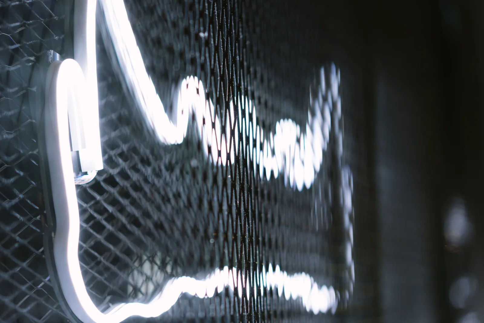 Close-up of a glowing neon sign with a wire mesh background, creating a modern, industrial feel. CSA vs UL Electric Signs: What Canadian Sign Shops Must Know